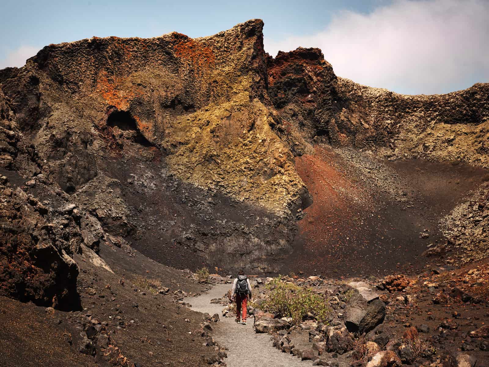 𝘐𝘮𝘢𝘨𝘦 𝘋𝘦𝘴𝘤𝘳𝘪𝘱𝘵𝘪𝘰𝘯: Matt walks along a path through a volcano - with oranges, reds, browns, greens and natural earthy coloured rocks all around him. ⁣