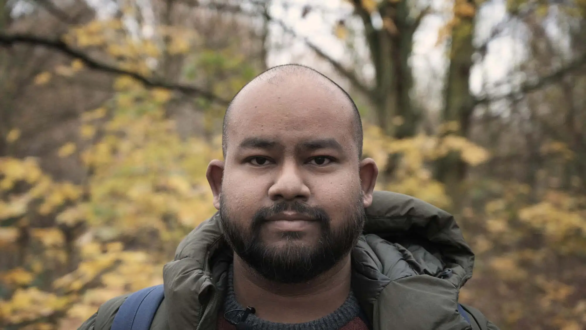 Image Description: A landscape format image. A head and shoulders portrait of Robi Choudhury in front of an out of focus background of trees.