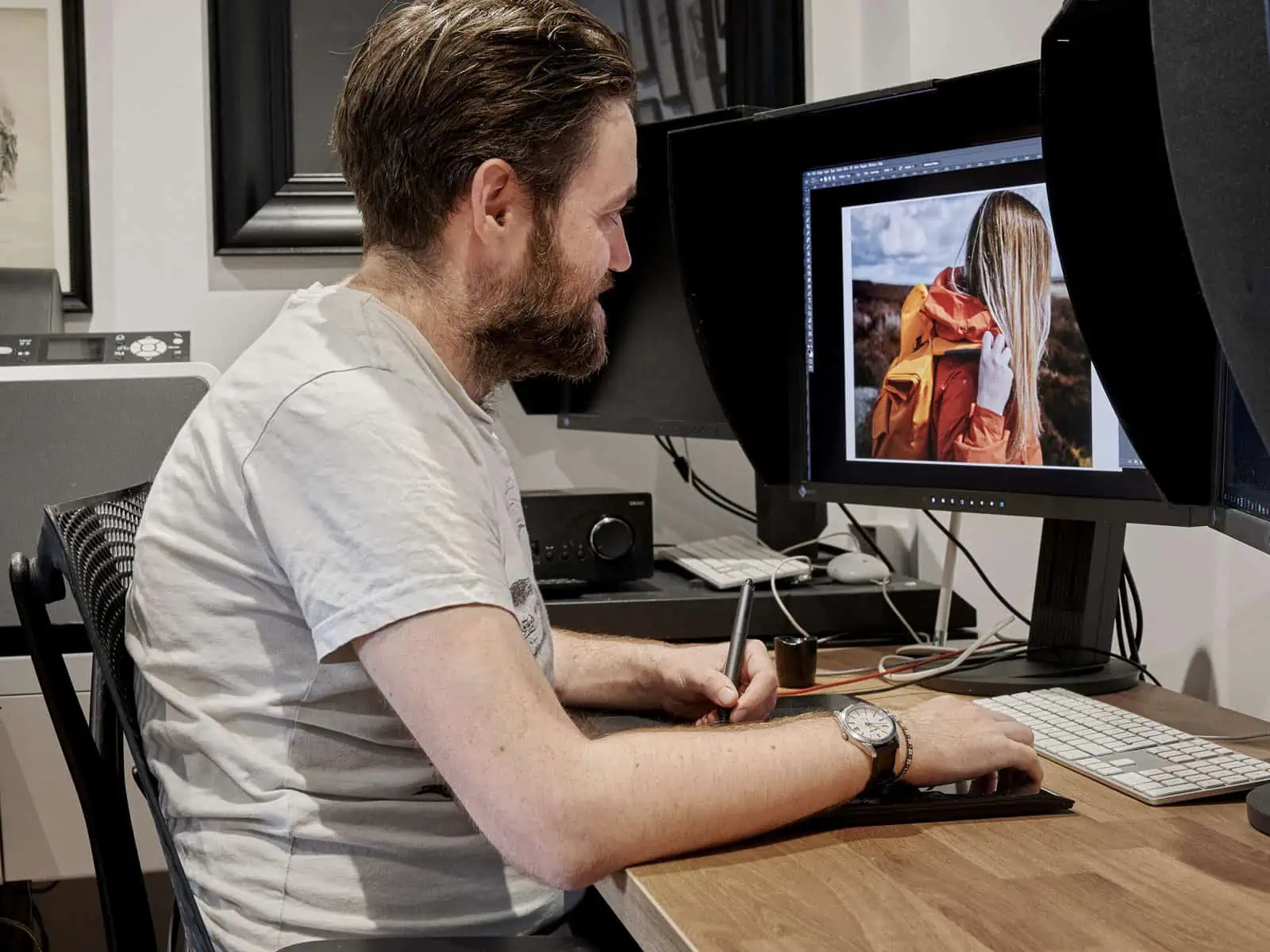 ID: A landscape image. Matt is sat at his desk working on an image at the computer. He is seen from the side. He is wearing a white tshirt.